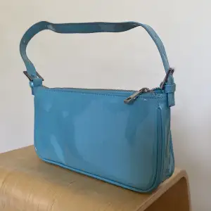 Blå handväska i lackmaterial från Gina Tricot. Använd ett fåtal gånger, men i gott skick. Mindre fläck på ena sidan som är ett fabriksfel.