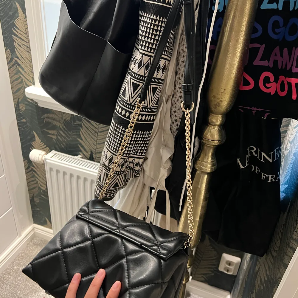 En svart handväksa som har guld ditaljer. Perfekt storlek enligt mig får plats med mycket 💕. Väskor.