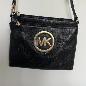Michael Kors väska - En svart väska i skinn från Michael Kors. Se slitningar på axelbandet samt metallen. Annars i fint skick. Praktisk väska med många fack!