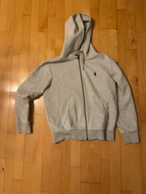 Ljusgrå Ralph Lauren zip-hoodie - En oanvänd zip-hoodie i storlek S som passar om man är 177-181 cm lång. Säljer en i samma model fast mörkblå till samma pris, men om man köper båda så får man dem för 2000 istället för 2200. Smsa om intresserad: 0700633245