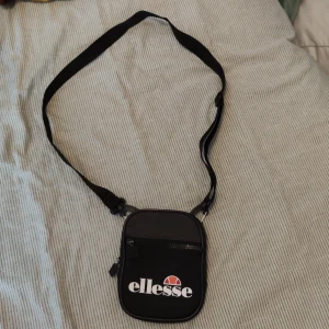 Ellesse midjeväska  - Ellesse midjeväska. Välanvänd men i bra skick. Dragkedjan till den lilla fickan är lite keff men fungerar bra. Det stora fickan har 2 fack, se bild 2. Kan även fästas på bälte, se bild 3. Bra för att bära runt på ditt snus och annat godis 🤗