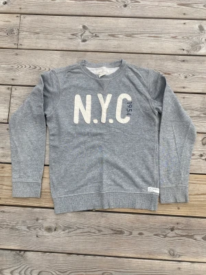 Collegetröja  - Gråmellangetröja med patchworktext. Mjuk, skön kvalle i bra skick. 