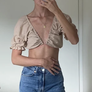 Beige topp - Fin beige topp med puffärmar, resor runt och snörning som man kan både knyta bak och framtill. Djup ringning. Från Bikbok i storlek S