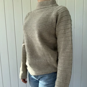 Stickad Tröja  - En randig stickad tröja i färgen beige med hög krage. Håller dig varm och är snygg. 