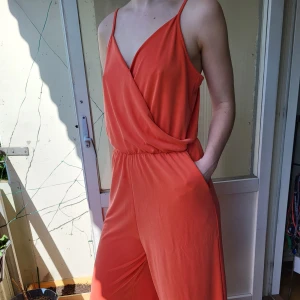 Orange byxdress - Somrig byxdress som passar lika bra till en dag i staden, som en middag på restaurang. Luftig och rörlig, stl M men passar en L (möjligen även en XL beriende på hur man vill att den ska sitta). Något kortare i modell - ankellängd