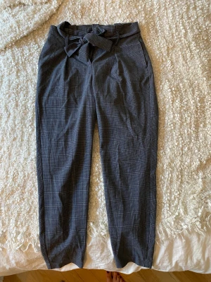 Rutiga kostymbyxor only - Raka rutiga kostymbyxor från only. Gråa. Skärp med knyte i rosett framtill. Storlek 36.