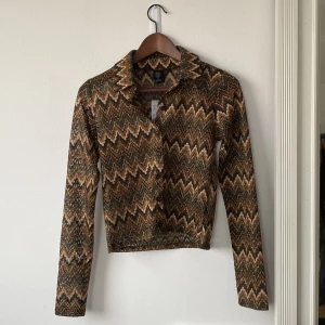 Urban outfitters skjorta - En brun, grön, orange skjorta ish med inslag av guld, helt oanvänd, från Urban outfitters. Storlek M men väldigt liten i storleken