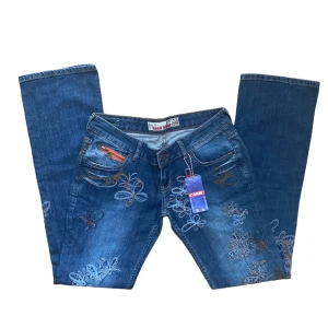 vintage broderi y2k jeans - coola broderade jeans med lapparna kvar. Lowrise och straight leg. Helt nya med lappar kvar! Strl på lapp säger W29, L33. Men måtten är: Midja: 74 cm, Innerbenslängd: 85 cm. Ytterbenslängd: 104 cm. Köparen står för frakt. ‼️  