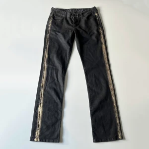 Svarta jeans - Svarta lågmidjade jeans från IKKS med guldfärg på sidorna. Midjemått: 76 cm, stretchiga. Innerbenslängd: 86 cm. Jag är 176 cm