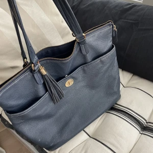 Tommy hilfigher väska  - En Tommy hilfigher väska köpt i USA för något årsen! Säljer då den inte kommit till användning, de är hål i tyget på botten men går enkelt att laga med nål och tråd (inget som märks heller) 💙 jätterymlig och perfekt till skolan/jobb!