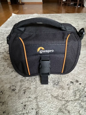 Kameraväska  - - Väderskyddad design med regnsäkert lock - Löstagbar hängspänne - Många fickor och fack - Passar till en kompaktkamera med objektiv, videokamera eller actionkamera.  Bredd 20 cm Höjd 13 cm Djup 13 cm