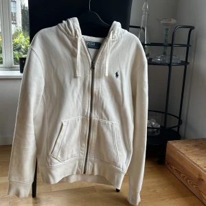 Ziphoodie Ralph Lauren - Vit ziphoodie med grönt märke. Lätt missfärgad vid kragen och inuti luvan. Mindre stänkfläckar på armarna och vid fickan samt ena mudden (hör av för fler bilder). Väldigt prisvärd. Köparen står för frakten. Säljs pga för liten.