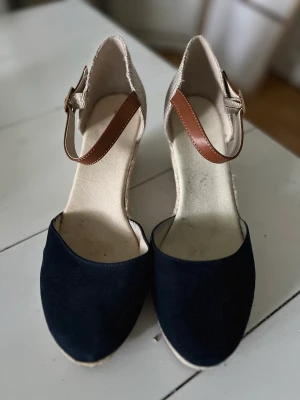 Skor med kilklack - Fina skor med kilklack, endast använda en gång. Mörkblå och beiga med brun rem,