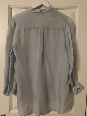 Ljusblå blus  - Lite silkesliknande material, superfin att ha under en stickad tröja tex! 