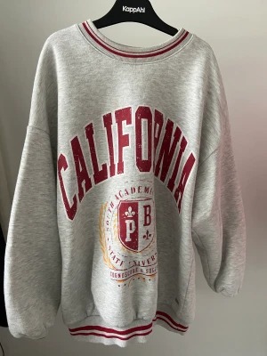 Collegetröja med tryck - Grå oversized collegetröja från pull&bear. Rött och gult tryck på framsidan, röda detaljer. Ganska bra skick.