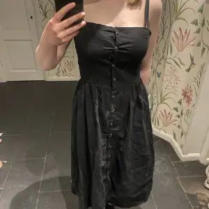 En svart lång klänning som är väldigt fin och kan användas speciellt på sommaren! Den är i bra skick och knappar som går längst hela klänningen. 