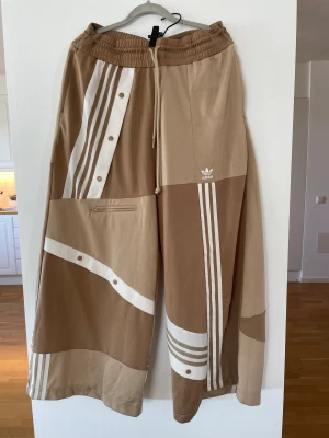 Adidas x Danielle Cathari  - Säljer mina superbekväma spaciga Adidasbyxor. Strl L men passar en M med. Passar en som är ca 160-166 cm lång.  Några små fläckar på ena benet men syns knappt. Köpta på plick! 
