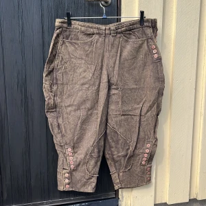 Unika byxor - Ett par brunskiftande vida byxor med knappdetaljer samt knappstängning i sidan. Har 4 fungerande fickor. 100% bomull.