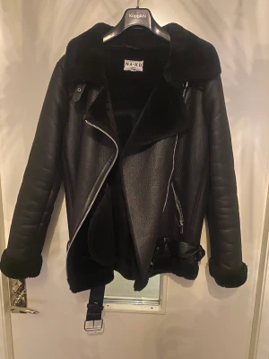 Fodrad skinnjacka  - Fodrad skinnjacka från NA-KD, funkar perfekt som en snygg jacka både under höst och vinter. Säljer pga använder en annan jacka denna vinter. Strl 38 men med tjock tröja under skulle jag säga en 36. Jag är ca 170 och på mig går den till rumpan
