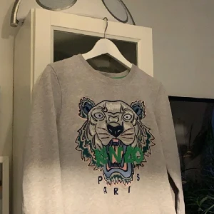 Kenzo tröja grå - Säljer denna fina kenzo tröjan som ser ut att vara i nyskick. Har inte använt den på flera år sen den har bara legat fint ihopvikt i garderoben. Inga fläckar eller skromer. Är köpt på NK för ca 2300 kr. Är i storlek M.