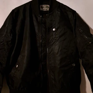 Svart Bomberjacka  - Svart bomberjacka med en ficka på ena ärmen.Säljer på grund av att den är alldeles för liten.Fick den i present. Använd öppen en gång.Är storlek small.
