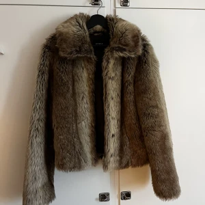 Pälsjacka, Lindex - Inte äkta päls. Nyskick. Fint brunt innerfoder. Varm. Går att knäppa ända upp i kragen.