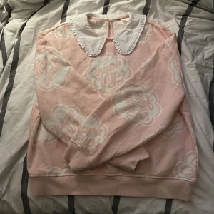 Rose tjocktröja med krage - Rosa tjocktröja med chups chups logan på. Insidan är super mysig och kragen är inte obekväm. Storleken är S men borde passa M och kanske till och med L? Den ska vara “loose fit”.