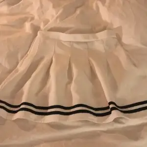 En kort kjol med 2 svarta sträck längst ned. Bra i skick. Vet tyvärr inte märket