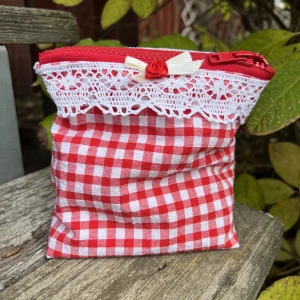 Necessär röd - En röd och vit handgjord necessär med söta detaljer samt dragkedja längst upp. Får plats med allt ifrån smink till bindor. Måtten är:  Höjd : 14cm  Bredd (mitten): 9cm Bredd (på botten):9cm Gjord i bomullstyg. Ligger även ute på tradera.skriv först:)