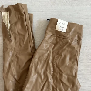 Byxor från zara - Oanvända byxor i skinnimitation med slits från zara i strl s. Helt oanvända och i jättefint skick, har enbart varit nedvikta i min garderob därav skrynkliga på bilderna.