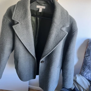 Kort kappa - Kort kappa från hm. I en jättefin grön grå färg. Väldigt unik har aldrig sett någon ha en likadan. Inget tecken på användning. 