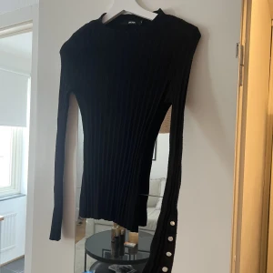 Tröja - Svart tight tröja i ribbat material. Fina guldiga knappar på ärmarna 