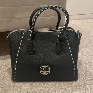 Guess svart väska  - Säljer denna guessväskan i ett väldigt bra skick! Den har två defekter där lädret har gått upp men är annars i ett väldigt bra skick💛