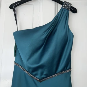 Balklänning - Säljer min fina balklänning :) Den är i siden & helt oanvänd, one shoulder & med fina detaljer i midjan & på axeln. I verkligheten är färgen mer smaragdgrön. Storlek s/36. Finns i Gbg att hämta men kan också skicka🥰