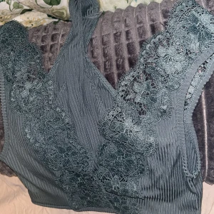 Grön spetsbody 🌿☘️🦖🪀🐛♻️🫑🐢🥦🧩🥒🪴🦠🌱 - Superfin grön spetsbody med djup urringning samt öppen rygg. Köpt för många år sedan så finns ej att få tag på längre, aldrig använd 💚