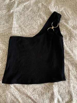 One shoulder top svart - Svart one shoulder topp med gulddetalj från Chiquelle, aldrig använd. Storlek XS. Cropped.