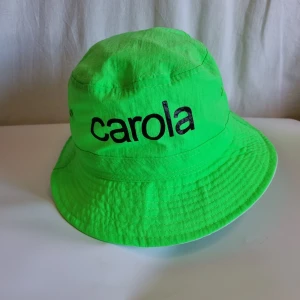 CAROLA HÄGGKVIST hatt buckethat fiskarhatt - Neongrön hatt med Carola tryck Hatten är vändbar One size/ en storlek passar alla  * Helt oanvänd * Officiell merchandise från turnén när det begav sig 