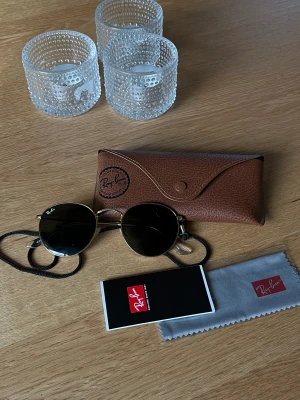 RayBan - RayBan solglasögon som jag köpt för flera år sen i butik. Fint skick. Guldiga runt om. Ingår  - Fodral till solglasögon  - Band till - Tvättduk (oanvänd och oöppnad) - Nån manual av nått slag