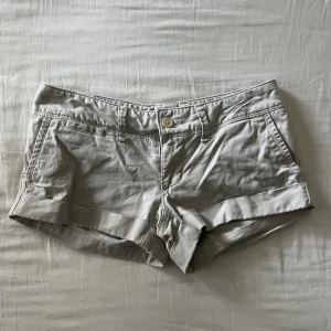 Beige-gråa vintage lågmidjade mini shorts - Supersöta vintage beige-gråa lågmidjade mini shorts med unika bakfickor. Begagnat skick, men inga fläckar eller hål! Midjemått mätt rakt över: 37cm, längd: 20cm. Storlek 34🫶💕