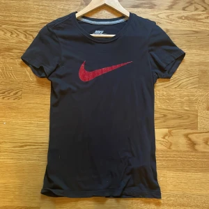Svart/mörk blå Nike T-shirt  - Svart T- shirt med röd nike logga. Luftigt tyg med bekväm passform.