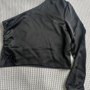 Blus med en ärm - En croppad satin blus med en lång ärm, rynkade detaljer vid axeln och på ena sidan.  ALDRIG ANVÄND! Enbart testad