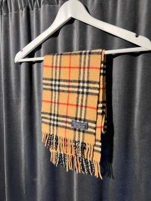 Burberry scarf - Fin Burberry scarf i en äldre årsmoddel, skick 9/10. Den är ungefär 106cm lång. 