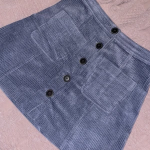 Blå Manchester Kjol - En blå kjol i Manchester tyg med svarta knappt framtill