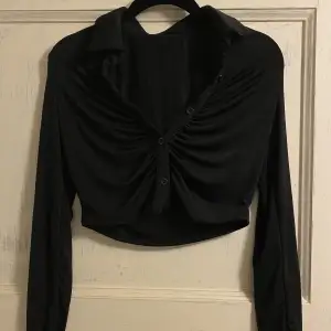 Croppad svart skjorta i glansigt men mjukt material. Aldrig använd. Strl xxs