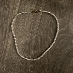 Pärlhalsband  - Pärlhalsband nytt. Tror det är gjort av plast, alltså ej äkta pärlor. Ca 49.5cm lång som störst och ca 44cm som minst. Detta är 2/3 pärlhalsbanden jag har lagt upp. Finns 3 totalt på sidan 