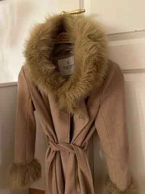 Beige vinterkappa  - Beige vinterkappa i storlek 34. Pälskrage i fuskpäls samt vid ärmsluten.  Rök och djurfritt hem
