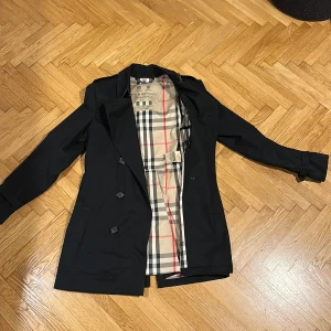 Burberry trenchcoat ”The Kensington” svart - Klassisk trench i svart, använd ett fåtal gånger, tidlös och riktigt bra kvalitet, köpt i gamla Burberry-butiken på Biblioteksgatan. Nypris 23 500 kr.