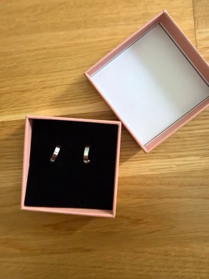 Snygga silvriga örhängen i box - Två par örhängen i silverfärg, ett par små hoops med slät yta men diamanter inuti. Kommer i en rosa presentask. Perfekta för dig som gillar minimalistisk och stilren design.