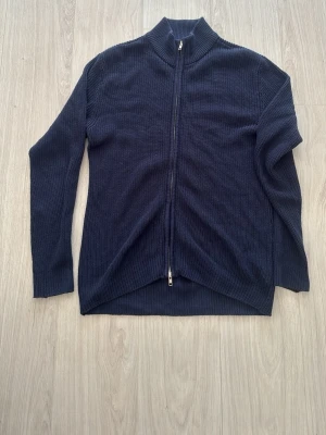 Mörkblå stickad ziptröja - Mörkblå stickad tröja med hel dragkedja framtill och hög krage. Tröjan har en ribbad struktur och är perfekt för lager på lager. Passar dig som gillar en enkel men stilren look.