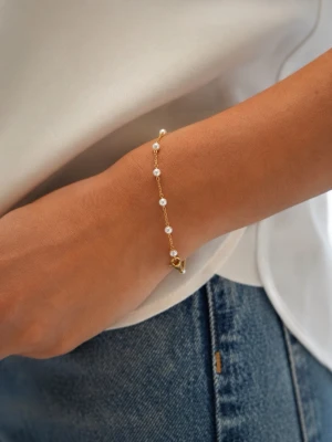 Guldfärgat armband med pärlor - Stilrent armband i guldfärgad metall med små vita pärlor jämnt fördelade längs en tunn kedja. Perfekt för dig som gillar minimalistiska och eleganta accessoarer. Lätt att matcha med andra smycken.